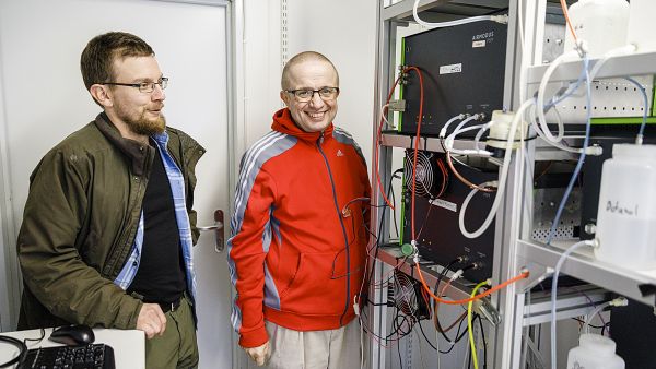 Tutkijatohtori Juho Aalto (vas.) ja akateemikko Markku Kulmala esittelevät yhtä Smear II -mittausaseman kopeista, jossa laitteet prosessoivat tutkimusmetsästä saatuja tietoja. (Kuvaaja: Seppo Samuli)