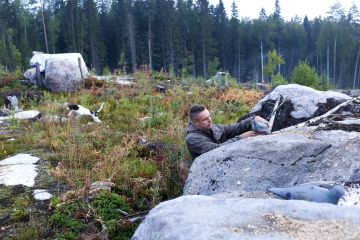 Samu Pekonen asettelee sepelkyyhkyjen houkutuskuvat kivenlohkareiden päälle. Lyhytkarvainen saksanseisoja Lumi ottaa ilon irti jahtiaamusta ennen passipaikalle asettumista. (Kuvaaja: Sami Karppinen)