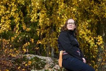 Mervi Haavisto istuu Papan huilauskiveksi nimetyllä kivellä. Siinä Haaviston isänisä piti usein lepotauon palatessaan metsätöistä kotiin. (Kuvaaja: Seppo Samuli)