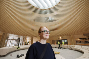 Arkkitehti Selina Anttinen aulatilassa, jonka LVL:stä valmistettua penkkiä fiksaillaan talven aikana tapahtuneen elämisen jäljiltä. (Kuvaaja: Seppo Samuli)